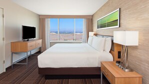 A hotel room with a large bed, a TV on a wooden desk, a lamp, and a view of the landscape through the window. - Holiday Inn Diamond Bar - Pomona by IHG (Diamond Bar)