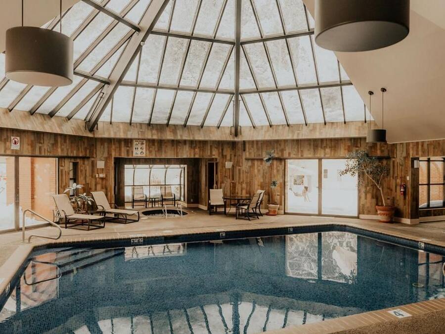 An indoor swimming pool with a glass ceiling, wooden walls, and lounge chairs.