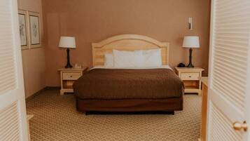 A hotel room with a large bed, two bedside tables with lamps, a wooden headboard, and a patterned carpet.