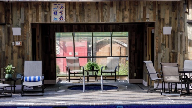 Zona de piscina con sillones de descanso, un jacuzzi y vista a un edificio rojo.