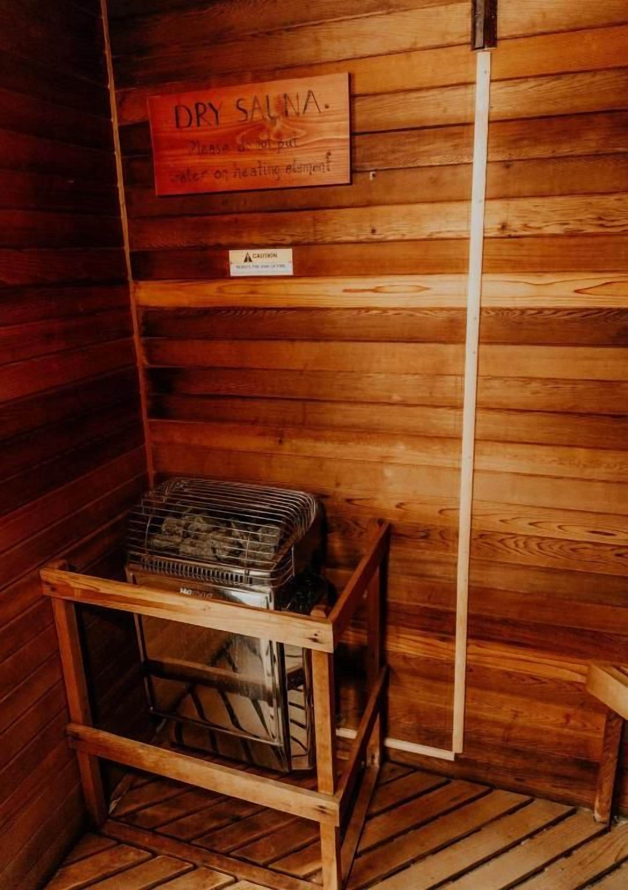 A wooden cabin with a sign indicating a dry sauna, a caution sign, and a metal rack with items.