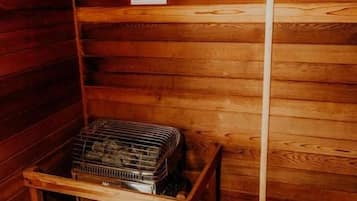 Cabana de madeira com placa indicando sauna seca, sinal de cautela e prateleira de metal com objetos.
