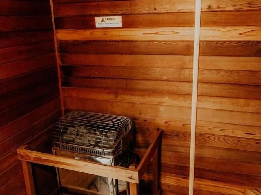 Cabana de madeira com placa indicando sauna seca, sinal de cautela e prateleira de metal com objetos.