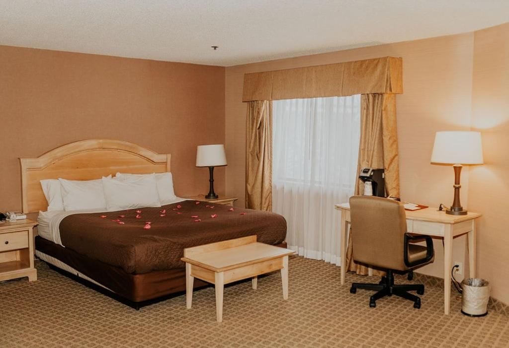 A hotel room with a bed, bedside tables, a desk, a chair, and a window with curtains.