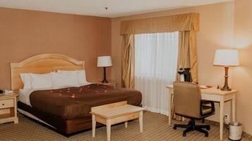 A hotel room with a bed, bedside tables, a desk, a chair, and a window with curtains.