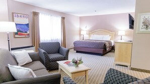 Habitación de hotel con cama, dos sillones, un sofá, una mesita con un florero, una lámpara y un cuadro en la pared.