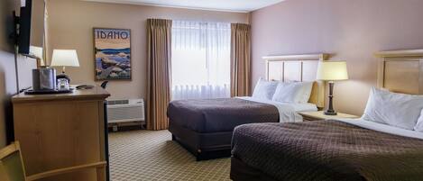 Una habitación de hotel con dos camas, un escritorio con lámpara, una silla y un cartel en la pared.