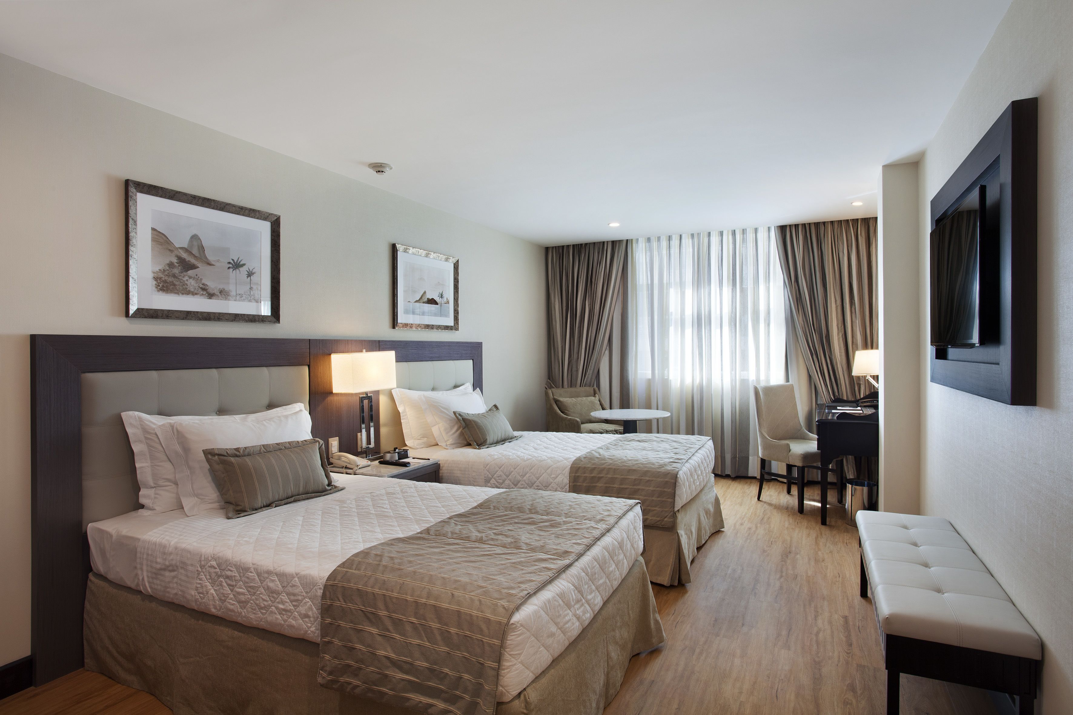 Quarto de hotel com duas camas, uma escrivaninha, uma cadeira e uma televisão.
