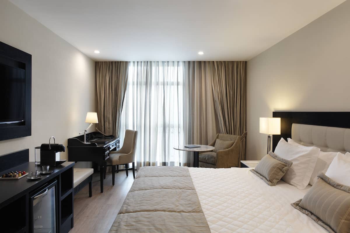 Una habitación de hotel con cama, escritorio con computadora, silla, televisión y ventana con cortinas.