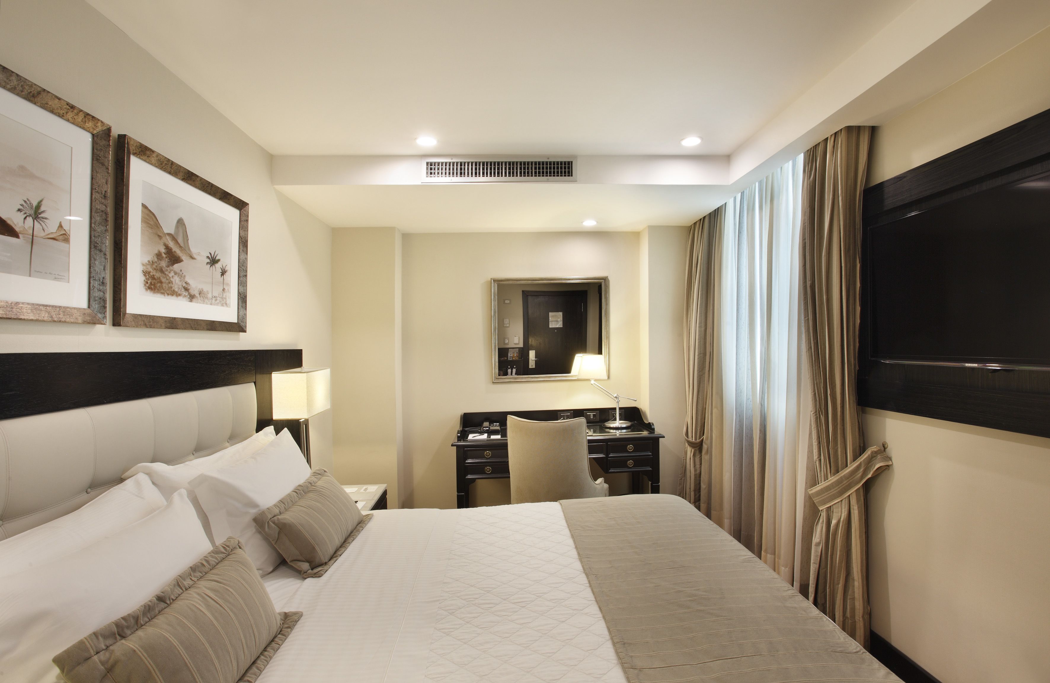 Quarto de hotel com uma cama grande, uma escrivaninha com cadeira, televisão e quadros na parede.