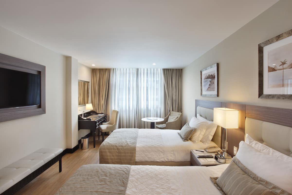 Una habitación de hotel con dos camas, un escritorio, una silla, una mesita y un televisor.