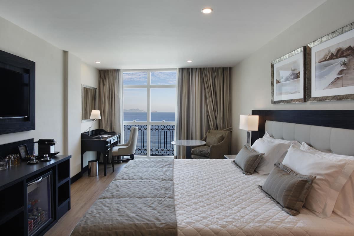 Habitación de hotel con una cama grande, un escritorio, una silla, un televisor y un balcón con vistas.