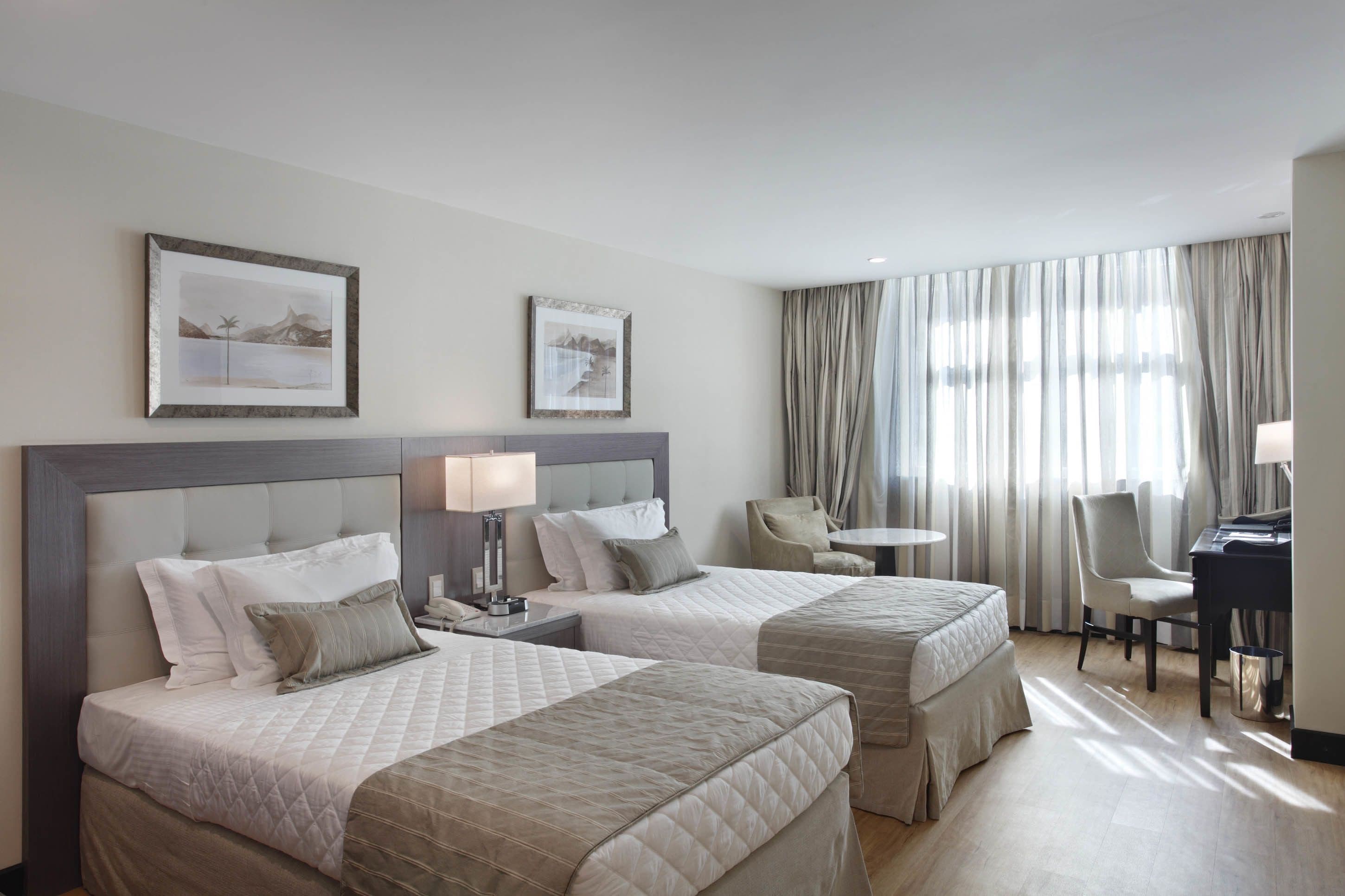 Habitación de hotel con dos camas, un escritorio, una silla y una mesita.