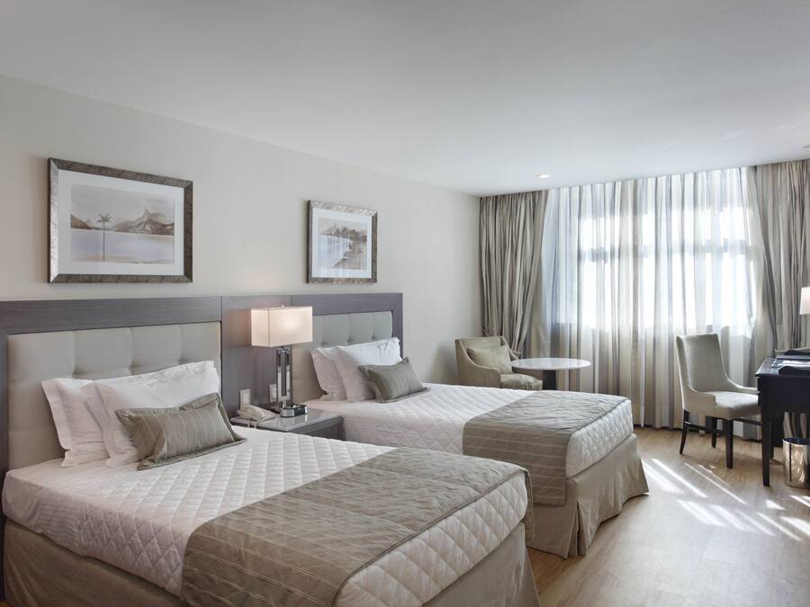 Ein Hotelzimmer mit zwei Betten, einem Schreibtisch, einem Stuhl und einem kleinen Tisch.