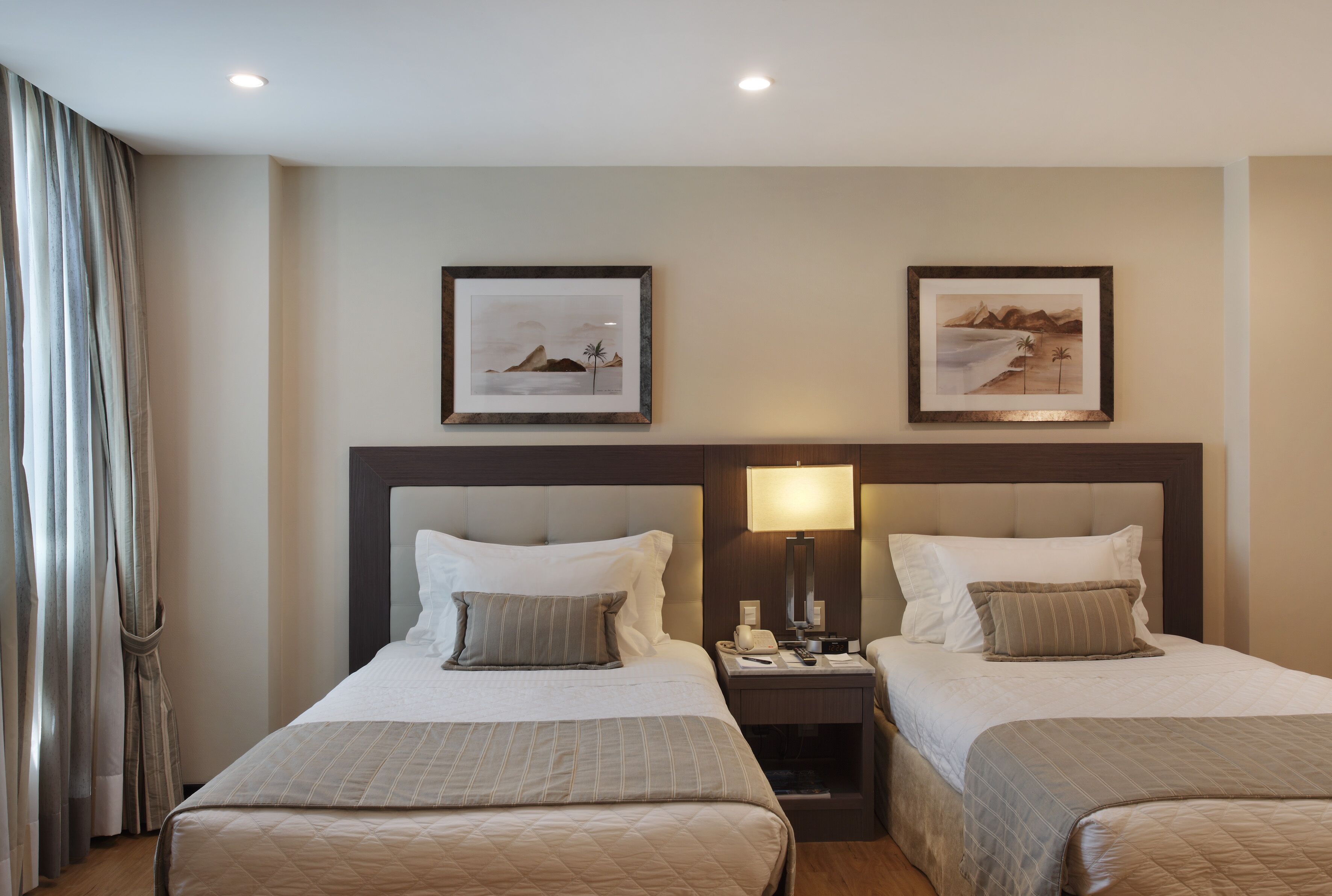 Une chambre d’hôtel avec deux lits, une table de chevet avec une lampe et des tableaux encadrés au mur.