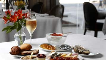 Uma mesa de jantar com diversos pratos, incluindo um croissant, queijo e ostras, além de uma taça de champanhe.