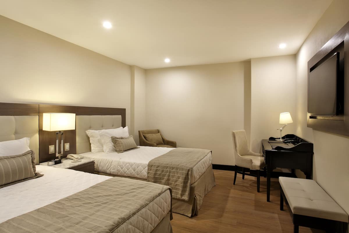 Habitación de hotel con dos camas, un escritorio, una silla, un televisor y un piano.