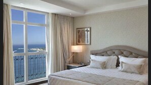Un cuarto de hotel con un ventanal grande, una cama con muchas almohadas, una mesita de noche y un cuadro en la pared.