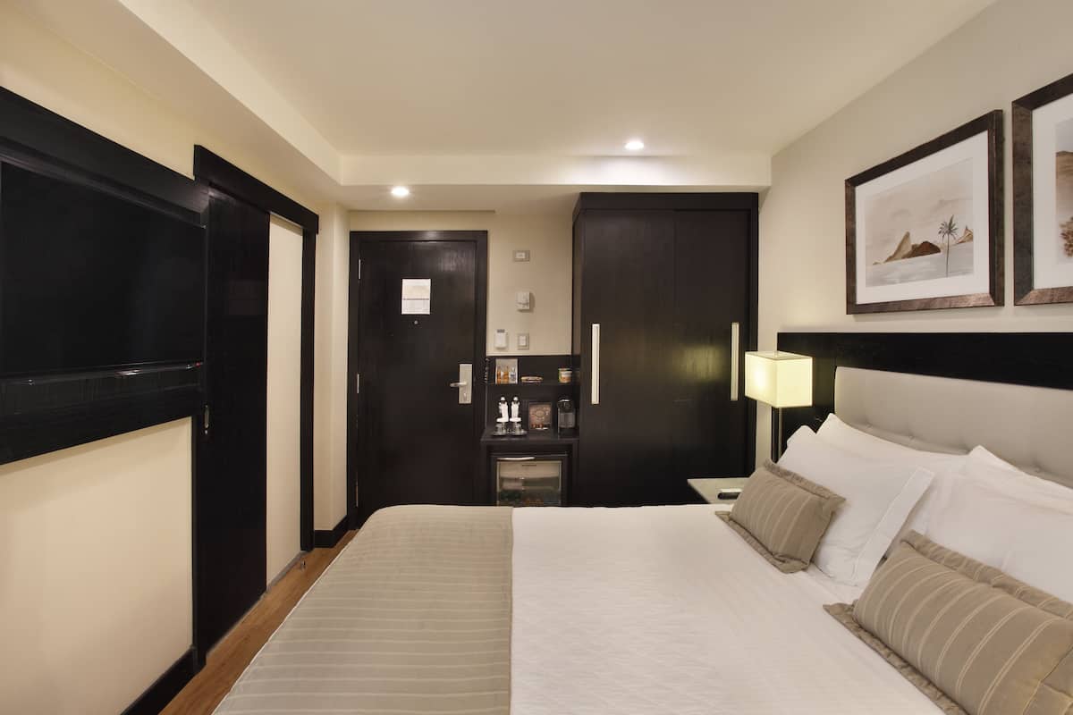 Una habitación de hotel con una cama grande, una mesita de noche, un escritorio, una silla, un armario, un espejo y una puerta.