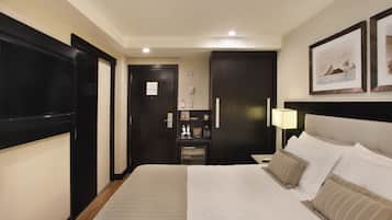 Hotelkamer met een groot bed, nachtkastje, bureau, stoel, kledingkast, spiegel en een deur.
