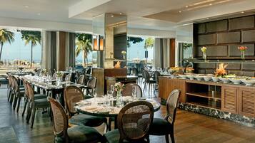 Un restaurante moderno con un amplio salón comedor, techos altos y grandes ventanales con vistas a la playa.
