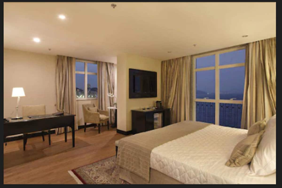 Habitación de hotel con cama, escritorio, silla, televisor y ventana con cortinas.