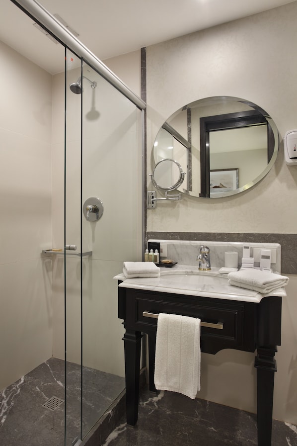 Une salle de bain moderne avec une douche à l’italienne en verre, un miroir rond, un meuble-lavabo noir avec un plan de travail blanc et un porte-serviettes.
