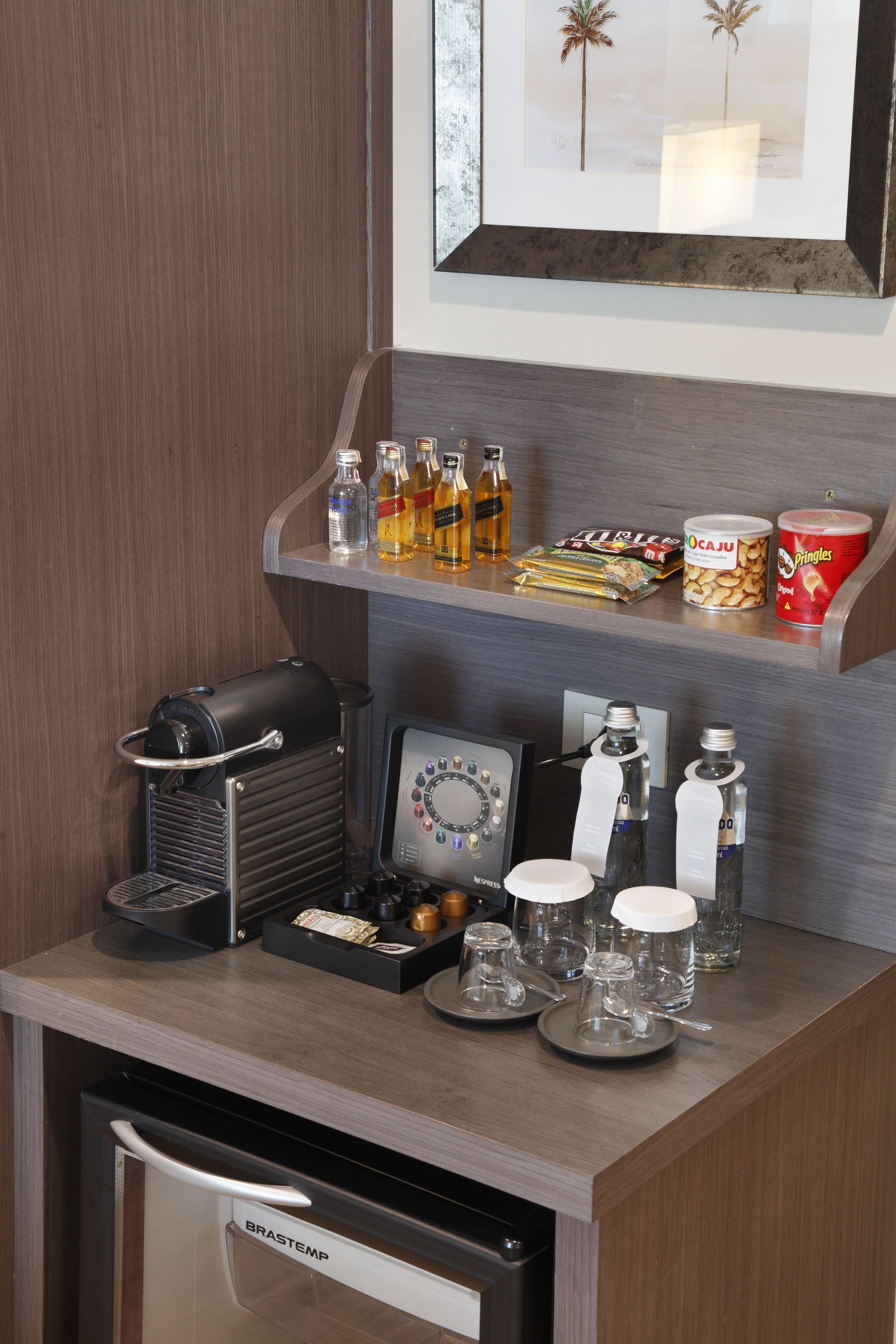 A kitchenette with a coffee machine, a mini-fridge, and various food and drink items on the counter.