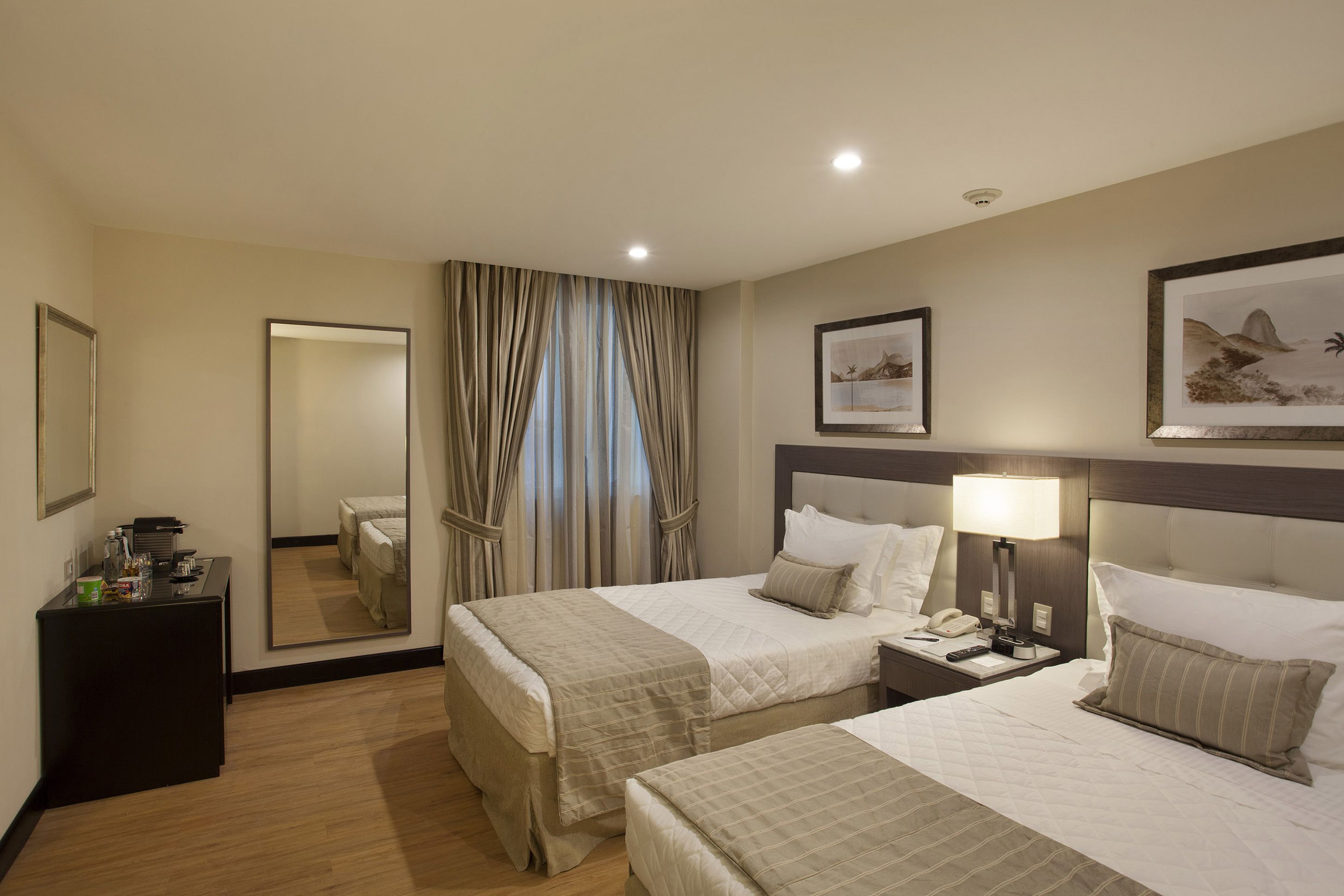 Une chambre d’hôtel avec deux lits, une table de chevet avec une lampe, un miroir et un bureau avec un téléphone.