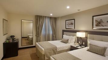 Une chambre d’hôtel avec deux lits, une table de chevet avec une lampe, un miroir et un bureau avec un téléphone.