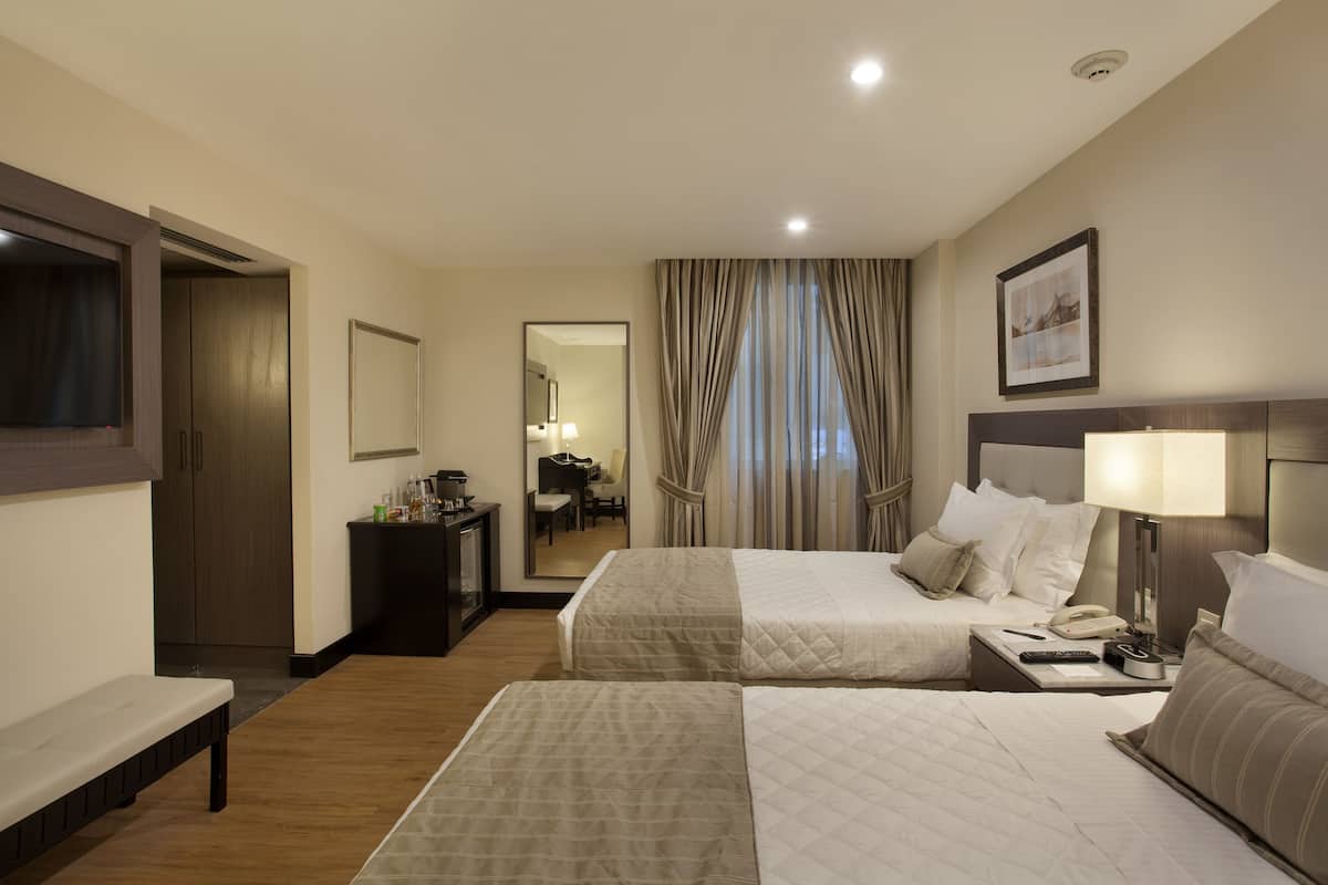 Una habitación de hotel con dos camas, un escritorio con lámpara, un teléfono y un espejo.