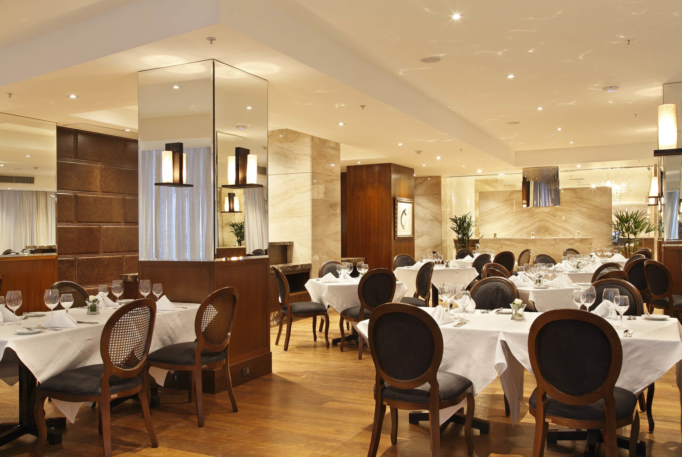 A restaurant with multiple tables and chairs, a wooden reception desk, and a marble wall.