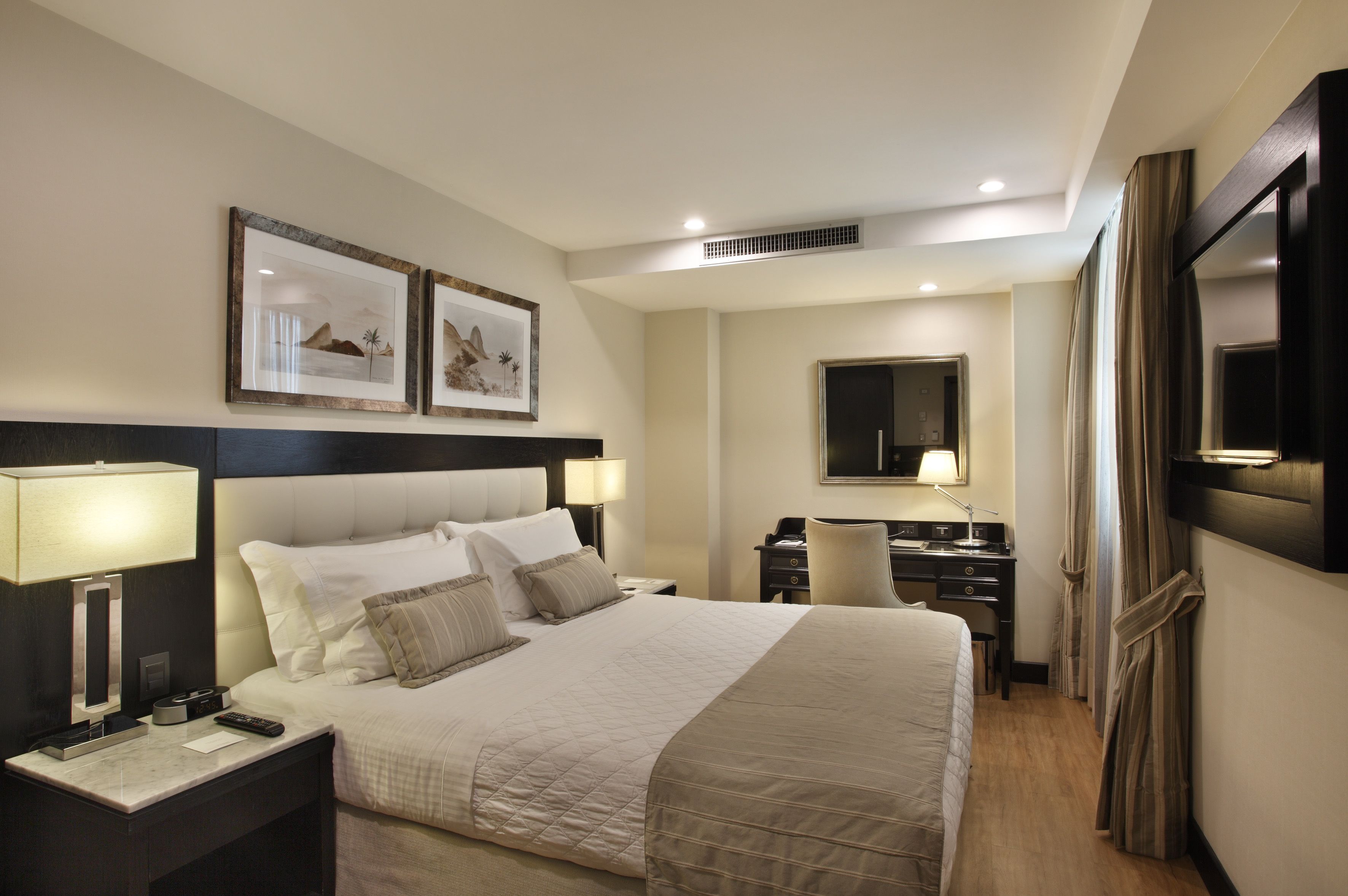Habitación de hotel con una cama grande, mesitas de noche con lámparas, un escritorio, una silla y un televisor fijado a la pared.