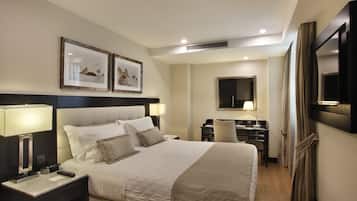 Habitación de hotel con una cama grande, mesitas de noche con lámparas, un escritorio, una silla y un televisor fijado a la pared.
