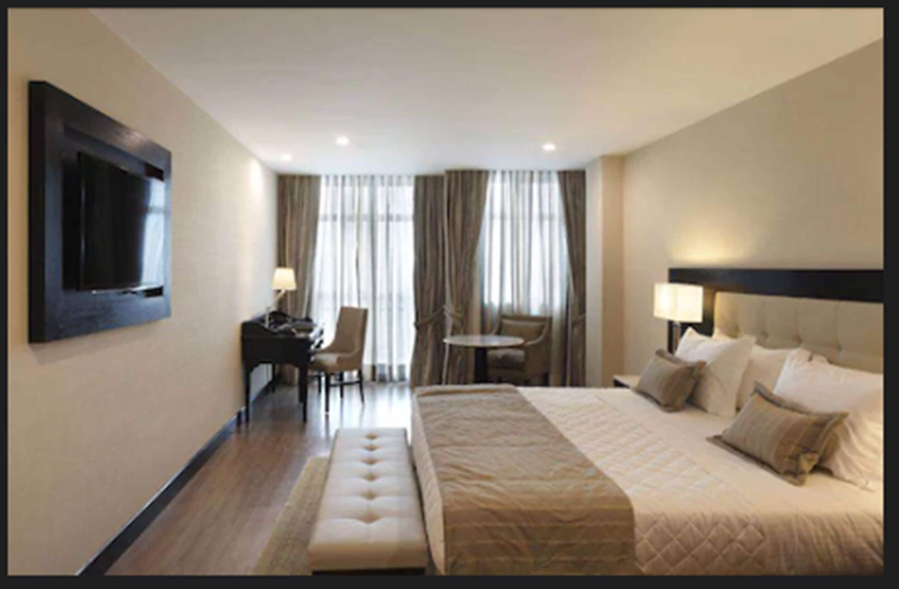 Ein Hotelzimmer mit einem großen Bett, einem Schreibtisch, einem Sessel und einem an der Wand befestigten Fernseher.