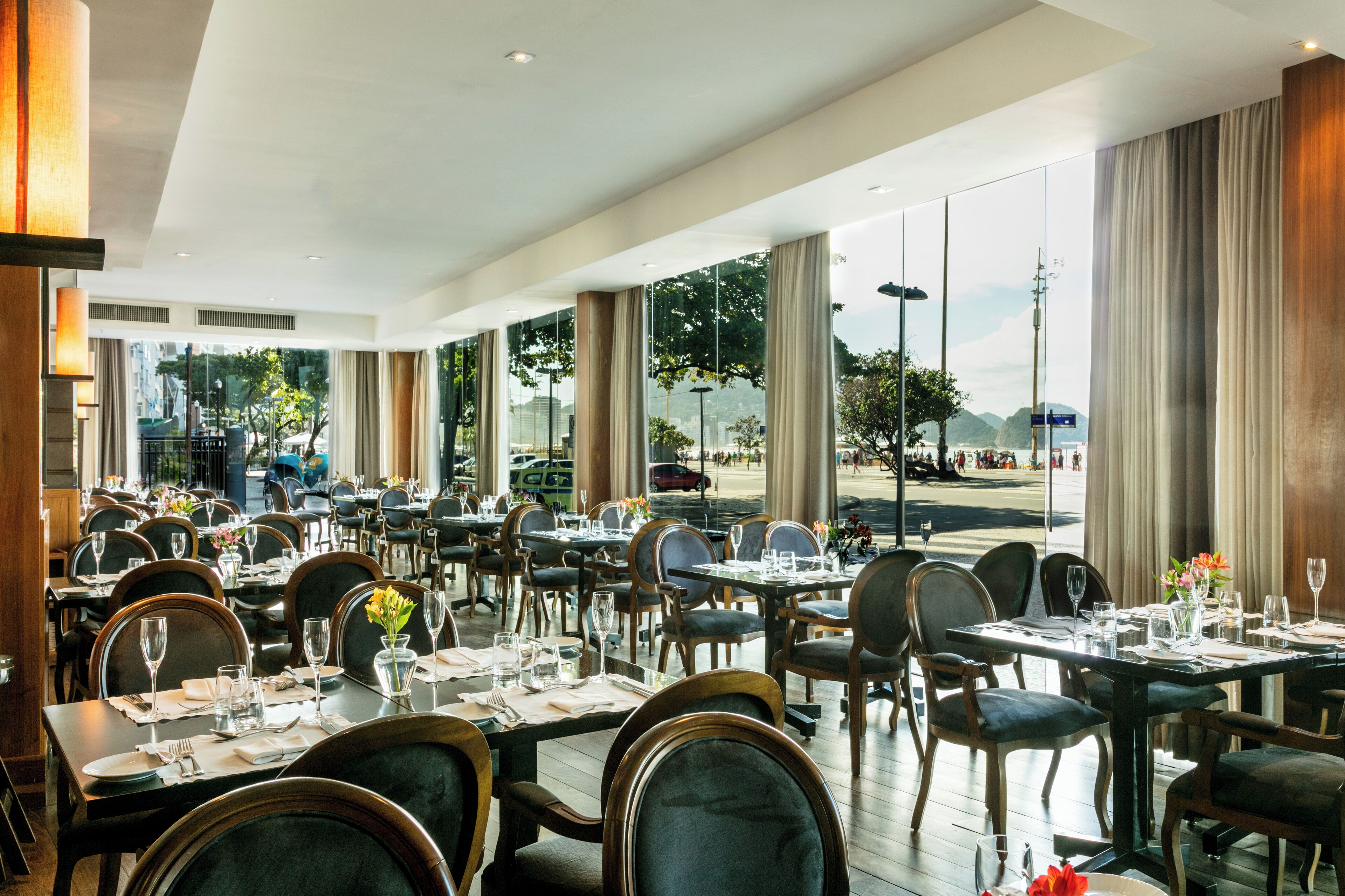 Un restaurante espacioso con varias mesas y sillas, amplias ventanas que ofrecen vistas al exterior.