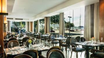 A spacious restaurant with multiple tables and chairs, large windows offering a view of the outdoors.