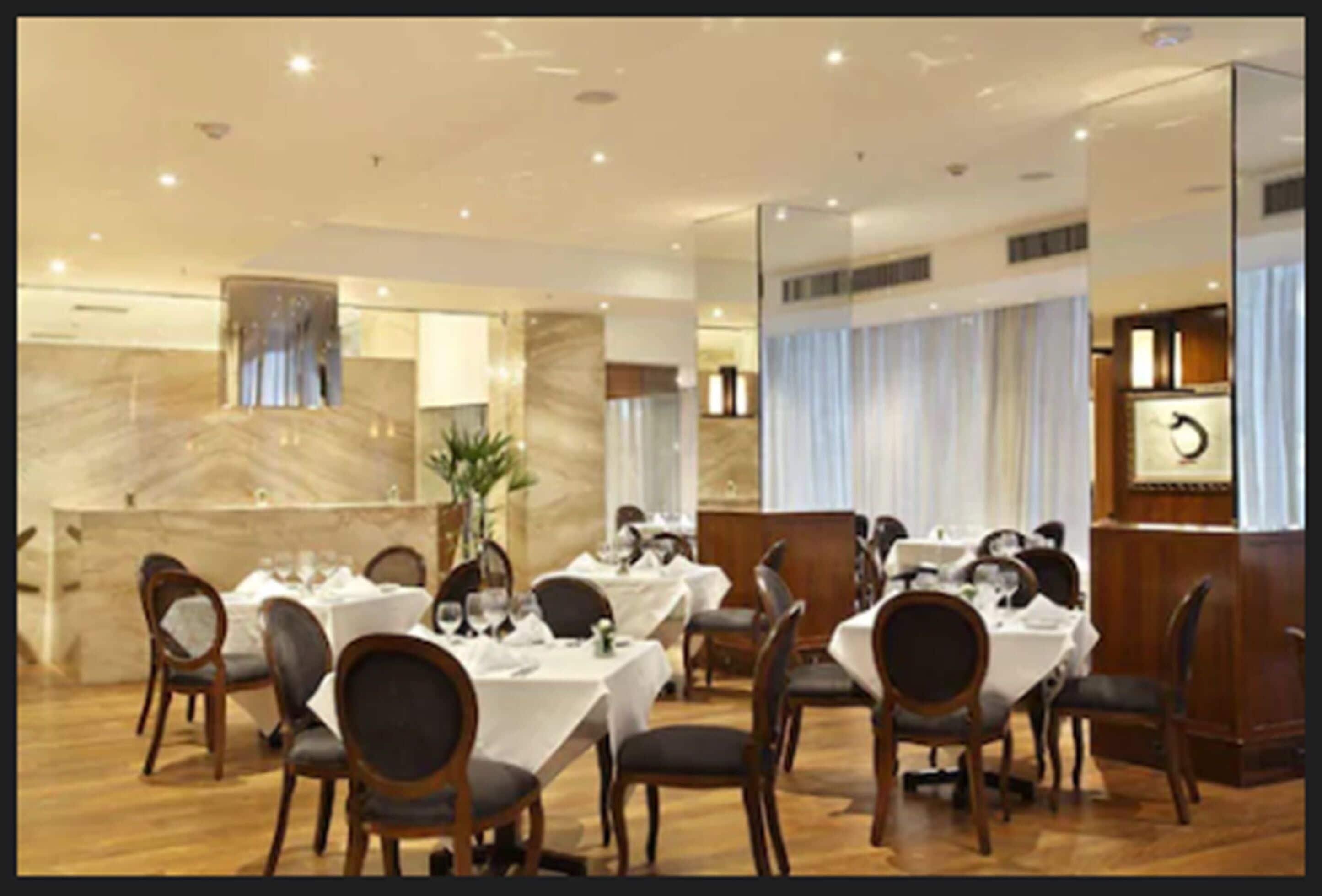 Une salle à manger d’hôtel avec plusieurs tables dressées, des chaises en bois et un mur en marbre.