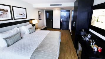 Une chambre d’hôtel avec un grand lit, une table de chevet avec une lampe, un téléviseur fixé au mur et un mini-bar contenant divers articles.