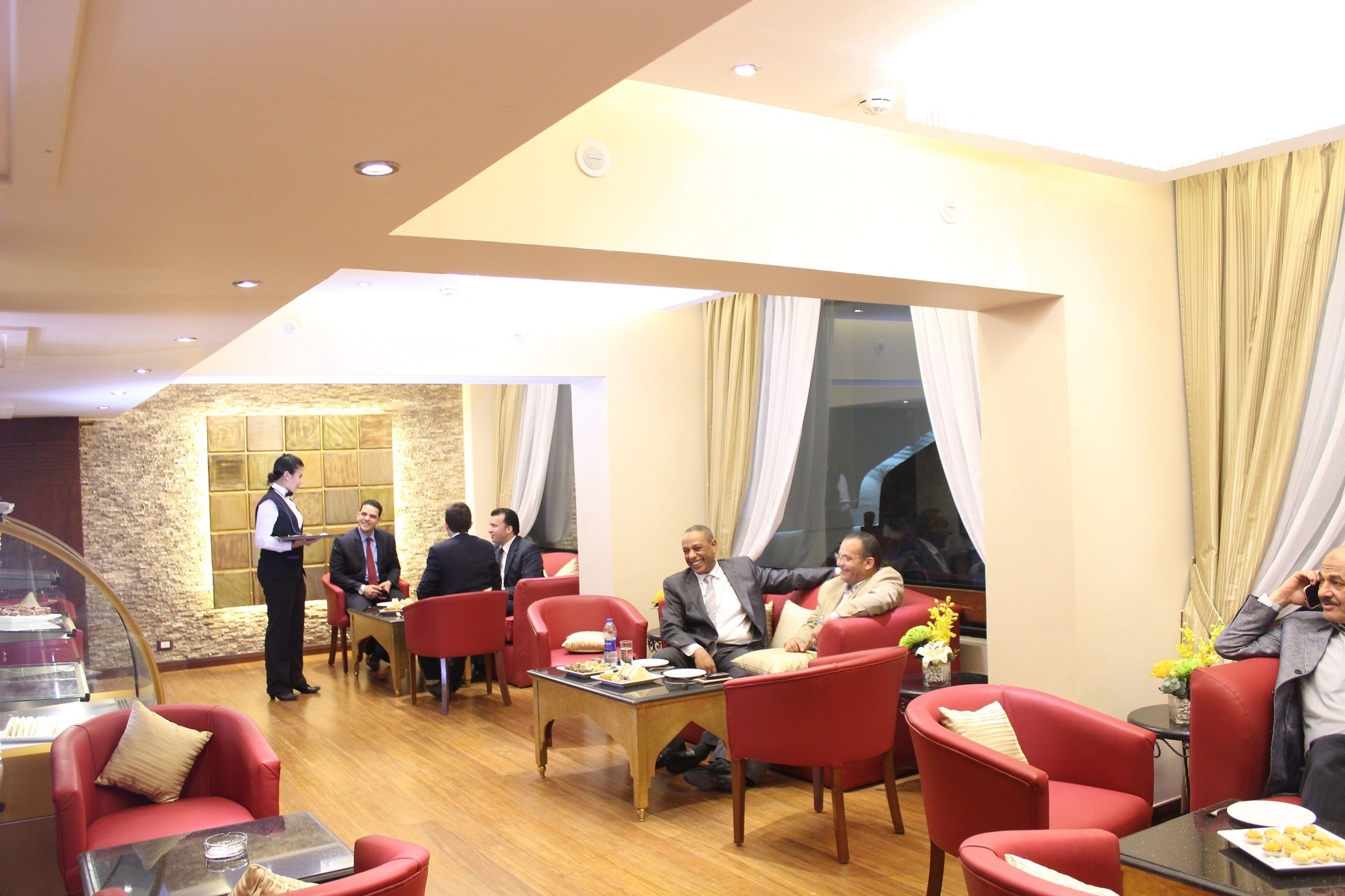 En hotellobby med röda sittmöbler, en servitör och ett område med en buffé.