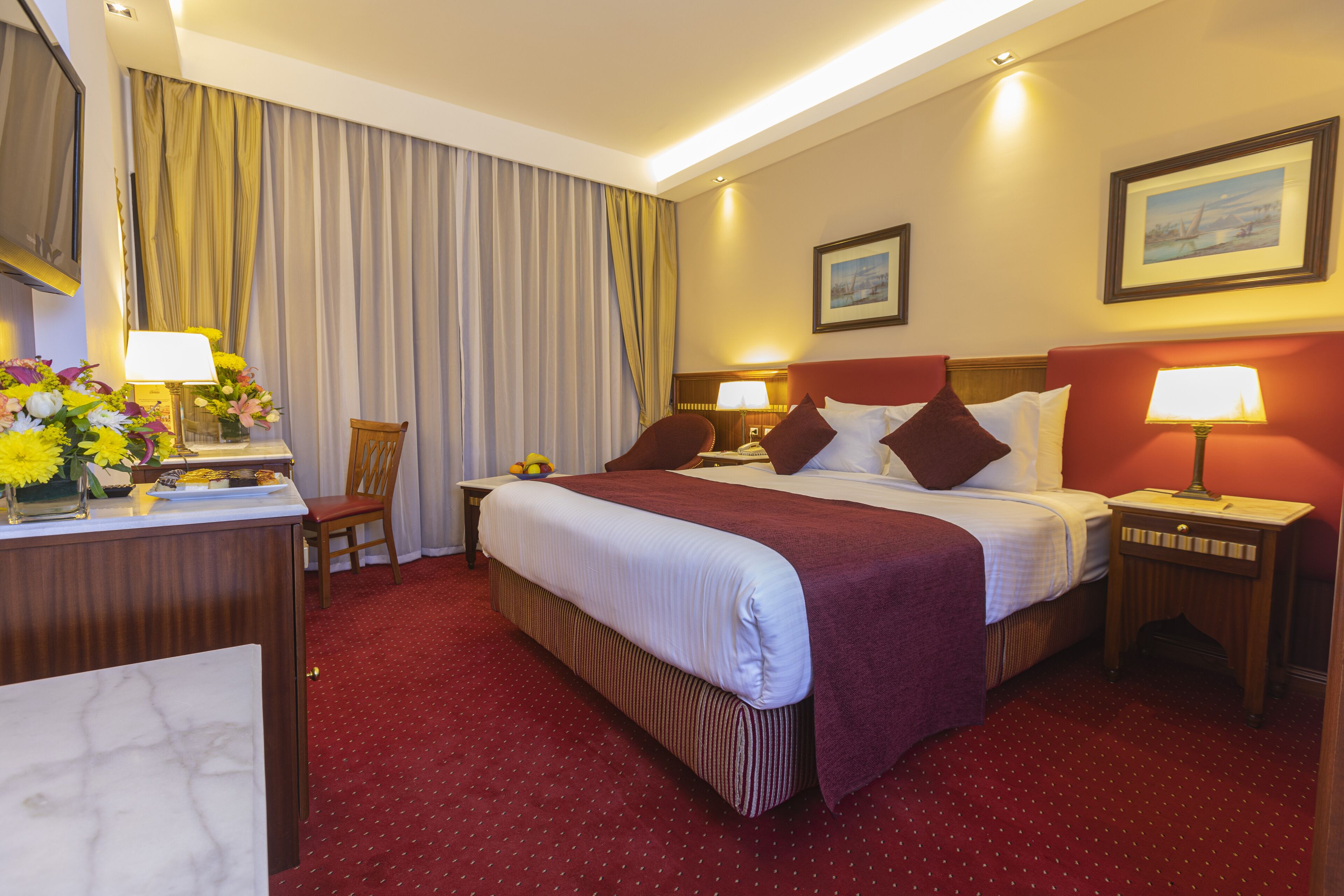 A hotel room with a large bed, two bedside tables with lamps, a desk with a vase of flowers, and a chair.