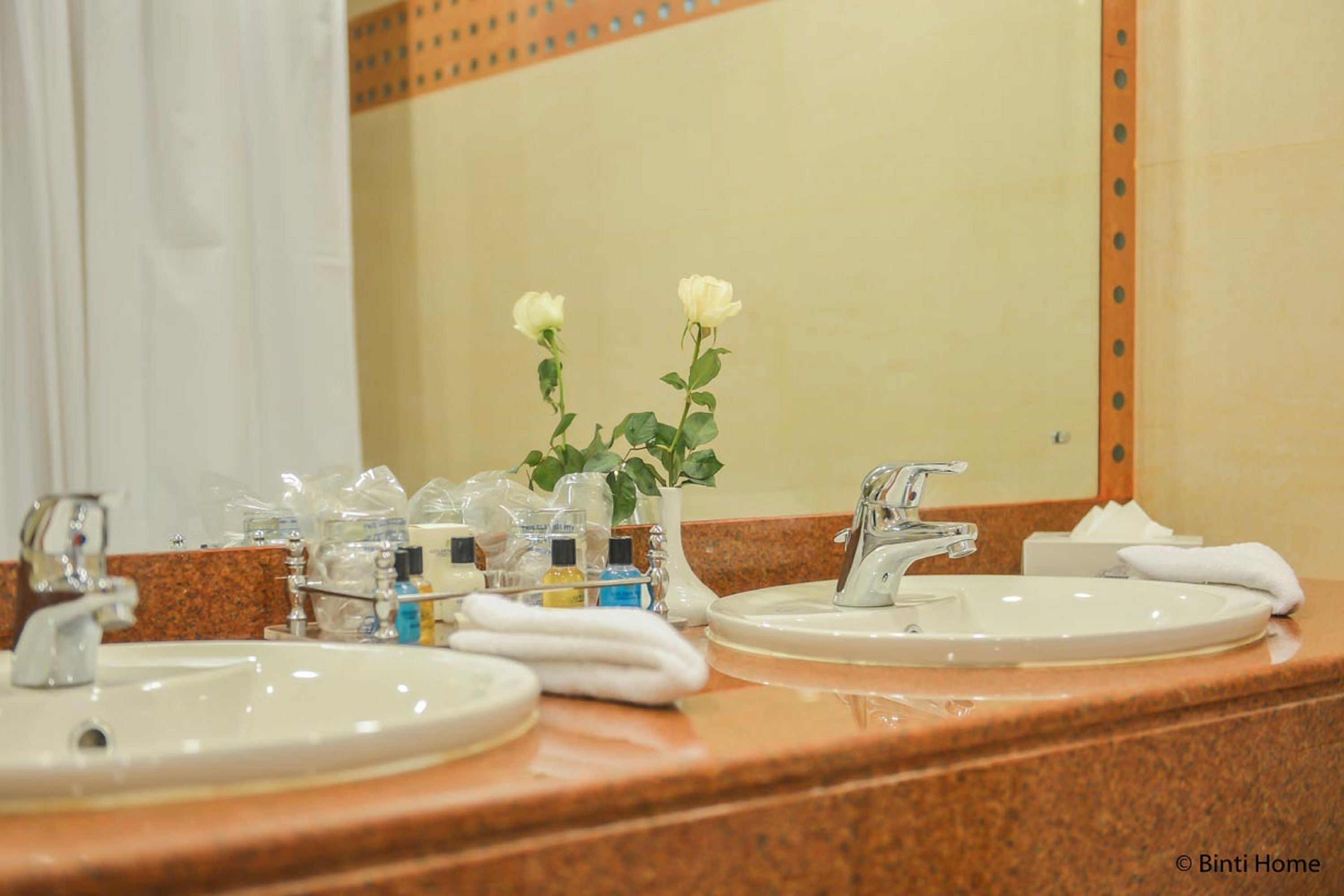 A bathroom with two sinks, a mirror, and toiletries on the counter.