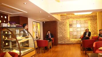 A modern hotel lobby with a bakery display, wooden flooring, and red seating.