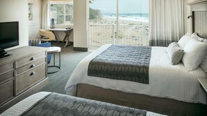A hotel room with a large bed, a desk, a TV, and a view of the beach. - Beachfront Inn (Brookings)