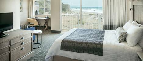 Ein Hotelzimmer mit einem großen Bett, einem Schreibtisch, einem Fernseher und Blick auf den Strand.