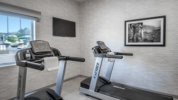 A gym with two treadmills, a water bottle on the left treadmill, and a framed picture on the wall.