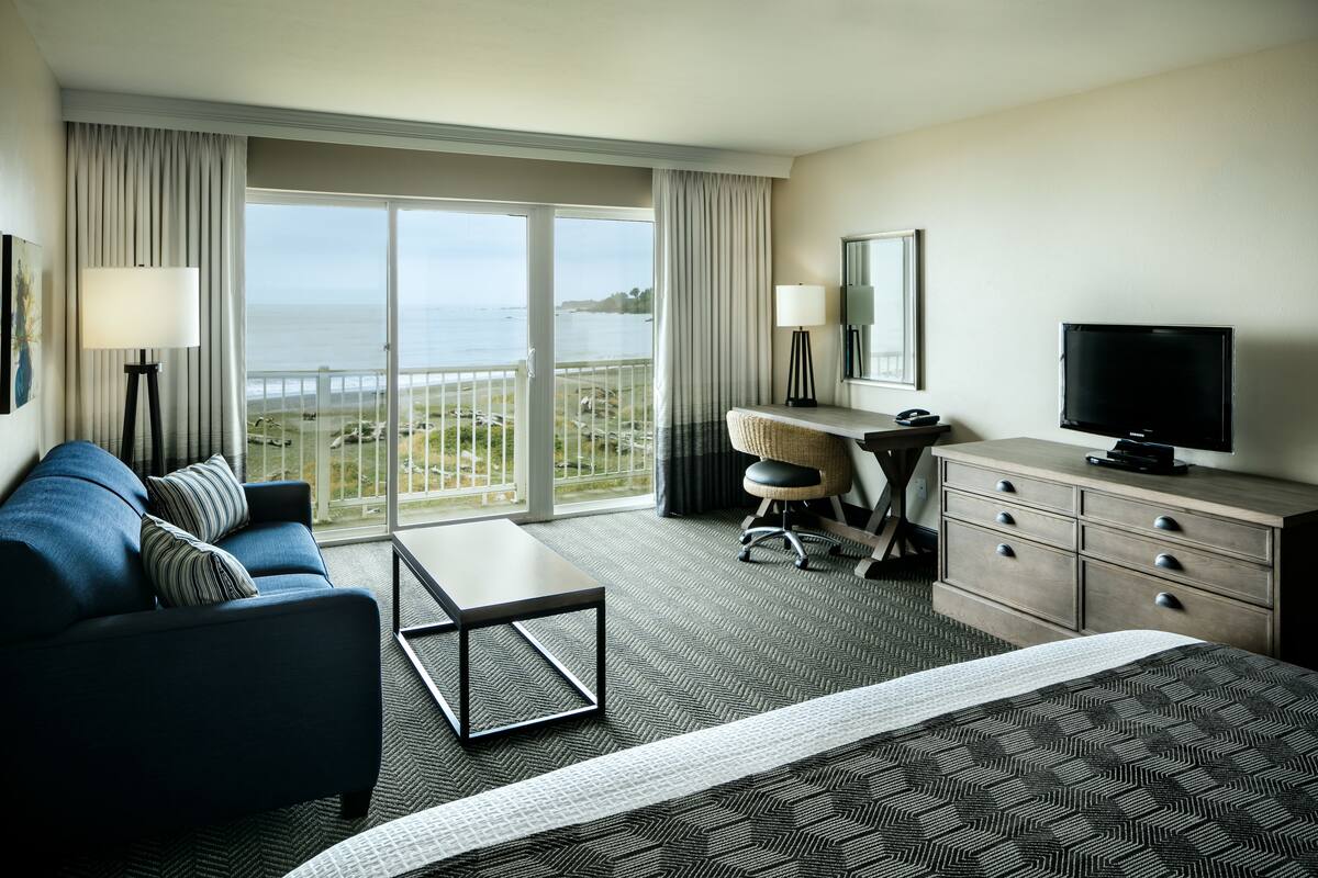 A hotel room with a bed, a desk, a chair, a TV, and a view of the ocean.