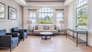 A spacious living room with a large arched window, a sofa, two armchairs, a coffee table, and a side table with a lamp. - Beachfront Inn (Brookings)