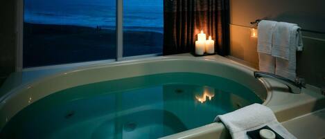 A bathtub with a view of the ocean, a towel, and candles.