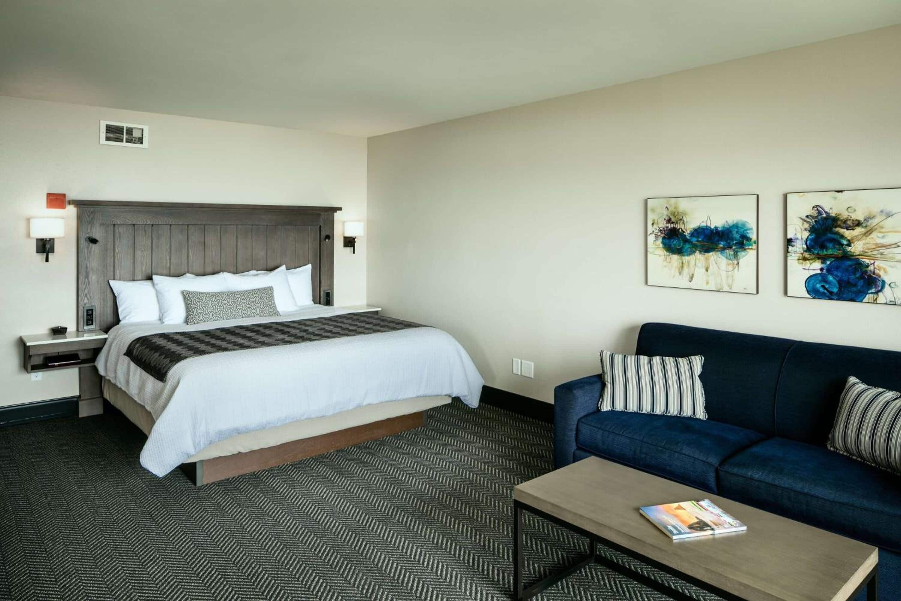 Ein Hotelzimmer mit Bett, einer Couch, einem Couchtisch und zwei an der Wand befestigten Kunstwerken.